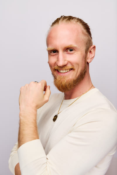 Fredrik Brännlund, founder of Noa The Game Fredrik Brännlund laughing with a closed fist at his chin, in a light knitted sweater